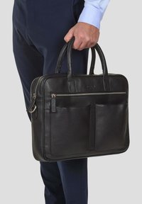 Sort læder arbejdstaske med to hanke, glat lynlåslukning, forlommer, struktureret overflade og sølvfarvede hardware-detaljer.
