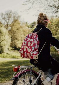 Een trekkoord rugzak in het rood met herhaalde konijnillustraties in wit, lichtblauw en roze. Gemaakt van stof met een gladde textuur.