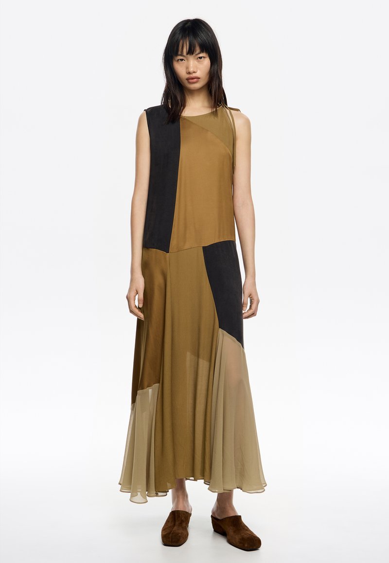 Sukienka maxi w brązowe i czarne bloki kolorów, z bezrękawową konstrukcją, warstwowym przezroczystym materiałem i zwiewnym dołem. Zamszowe brązowe buty.