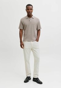 Polo a maniche corte marrone chiaro a motivo con colletto, abbinata a pantaloni color avorio e scarpe nere. Il tessuto presenta un design strutturato.