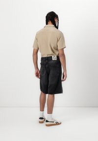 Beige kortærmet skjorte med krave, parret med sorte denim shorts med synlige baglommer og et mærke. Hvide sokker og sneakers.