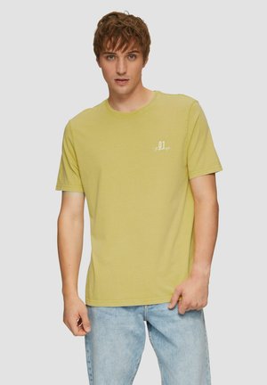 T-shirt en coton jaune clair avec un col rond et des manches courtes, arborant un petit motif imprimé blanc sur la poitrine. Associé à un jean bleu clair.
