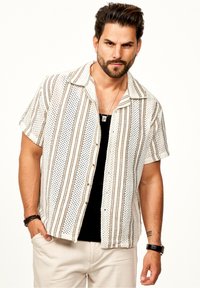 Kurzärmliges Hemd in Weiß mit braunen Streifenmustern. Verfügt über einen Kragen und eine lockere Passform, getragen über einem schwarzen Hemd.