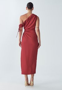 Asimetrisks sarkans kleita ar vienu plecu, izgatavots no gludas auduma, ar savilkamu mezglu uz pleca un pieguļošu vidukli, kas sniedzas līdz puslielam teļam.