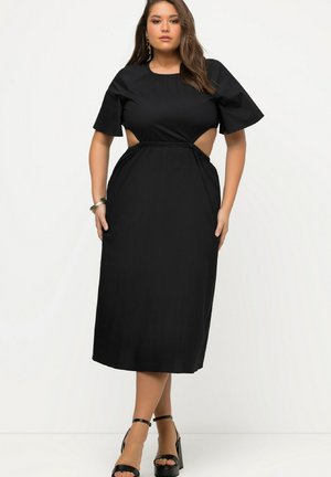 Abito midi nero con maniche corte e dettagli cut-out ai lati. Presenta una vita arricciata e un tessuto leggero. Abbinato a sandali con plateau.