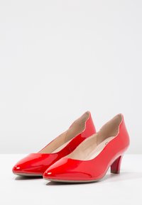 Chaussures à talons hauts en cuir verni rouge avec un bout pointu et un talon bas incurvé. L'intérieur présente une doublure beige lisse.
