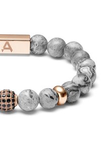 Perlesmykke med grå marmorert steiner, en gullfarget akzentperle, og en gravert gull rektangulær lås med bokstaven 'A'.