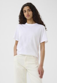 T-shirt bianco in cotone con scollo rotondo e maniche corte, vestibilità comoda, abbinata a pantaloni larghi chiari e testurizzati.