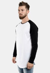 Langarm-Raglan-T-Shirt mit einem weißen Körper und schwarzen Ärmeln. Weicher Baumwollstoff mit rundem Ausschnitt und kontrastierendem Farbschema.