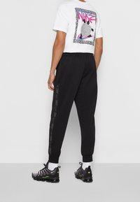 Svarta joggerbyxor med elastisk midja och avsmalnande ben. I kombination med en vit T-shirt med en färgglad grafisk tryck på baksidan.