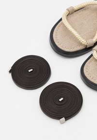 Sandali con tomaia in tessuto intrecciato beige, suole in gomma nera e doppie fasce arrotolate marroni scure con accenti in argento.