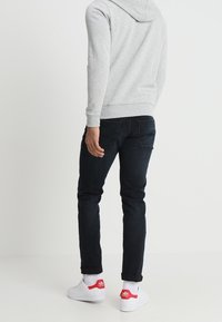 Grå hoodie med känguruficka, mörkblå jeans och vita sneakers med röda detaljer. Jeansens passform är slim och har uppvikta anklar.