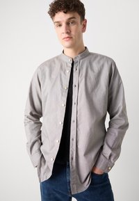 Lys grå knapp-up skjorte med bandkrave, med hvite knapper, lange ermer og en avslappet passform, paret med mørk denim jeans.