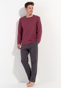 Röd och blå randig långärmad skjorta med rund halsringning, kombinerad med grå byxor. Materialet verkar mjukt, lätt och har en avslappnad design.