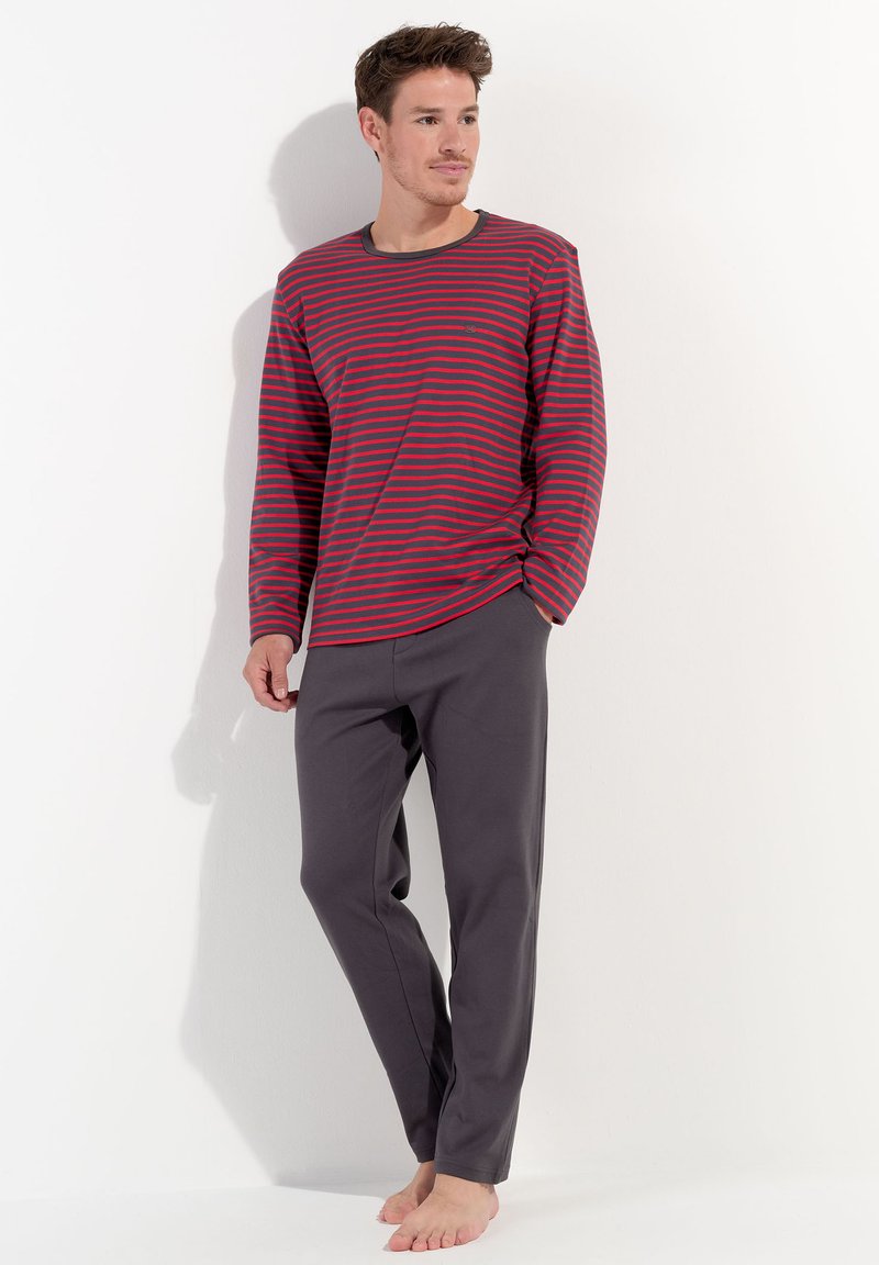 Camisa de manga larga a rayas rojas y azules con cuello redondo, combinada con pantalones grises. El material parece suave, ligero y de diseño casual.