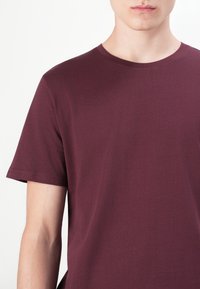 Bordeauxfarbiges Baumwoll-T-Shirt mit rundem Halsausschnitt und kurzen Ärmeln. Glatte Textur und minimale Nähte zeichnen es besonders aus.