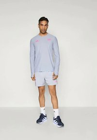 Lyseblå langermet skjorte og shorts med rosa detaljer, kombinert med mørke joggesko og hvite sokker. Minimalistisk atletisk design.