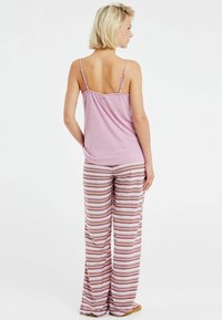 Lichtroze mouwloze top met dunne bandjes, gecombineerd met gemêleerde wijde broek in wit, bordeauxrood en roze zigzagstrepen. Glad textuur.