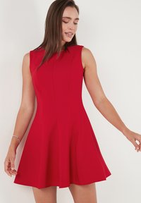 Red sleeveless dress with a flared skirt, made of smooth fabric. Features vertical seams and a fitted bodice, creating a structured silhouette.