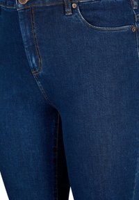 Jeans in denim blu scuro con cuciture arancioni, design aderente e stile classico a cinque tasche con bottone in metallo.