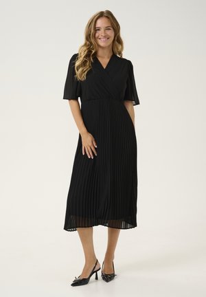 Black pleated dress with a wrap design and short, slightly puffed sleeves. Worn with black high-heeled shoes. Smooth fabric with a flowing silhouette.