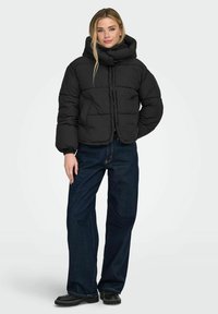 Sort dunjakke med høj krave og kort design, med puffede sektioner og frontlukning, kombineret med mørkeblå vidde bukser.