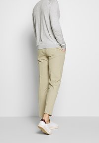 Camicia a maniche lunghe grigia chiara, pantaloni beige su misura e sneakers bianche con accenti maroon, visti da dietro. Texture liscia e design aderente.