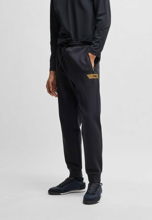 Pantaloni sportivi neri con vita regolabile, cerniera laterale e un accento in oro sul coscio sinistro. Tessuto morbido e liscio, vestibilità affusolata.