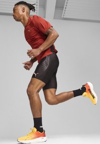 Camisa atlética roja de manga corta, pantalones cortos de compresión negros con líneas blancas y zapatillas de running con degradado naranja y calcetines negros.