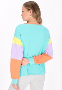 Maglione turchese a maniche lunghe con maniche a righe in tonalità pastello di giallo, viola e arancione. Texture liscia, vestibilità rilassata, scollatura rotonda con polsini a coste.