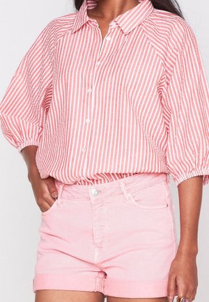 Mujer que lleva una camisa de botones a rayas verticales rosas y blancas con mangas abullonadas y pantalones cortos de mezclilla rosa claro con puños.