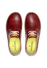 Zapatos de cuero marrón con la punta redondeada, que cuentan con cordones de color crema, plantillas verdes y un borde decorativo cosido.