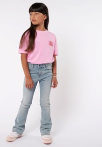 Rosa Baumwoll-T-Shirt mit dem Text "Lass uns das wieder machen", kombiniert mit hellblauen Schlagjeans und weißen/rosanen Sneakers, steht vor einem weißen Hintergrund.
