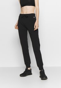 Schwarze Jogginghose mit Kordelzug in der Taille, verjüngten Bündchen und kleinem Markenlogo am linken Oberschenkel. Hergestellt aus weichem Baumwollstoff.