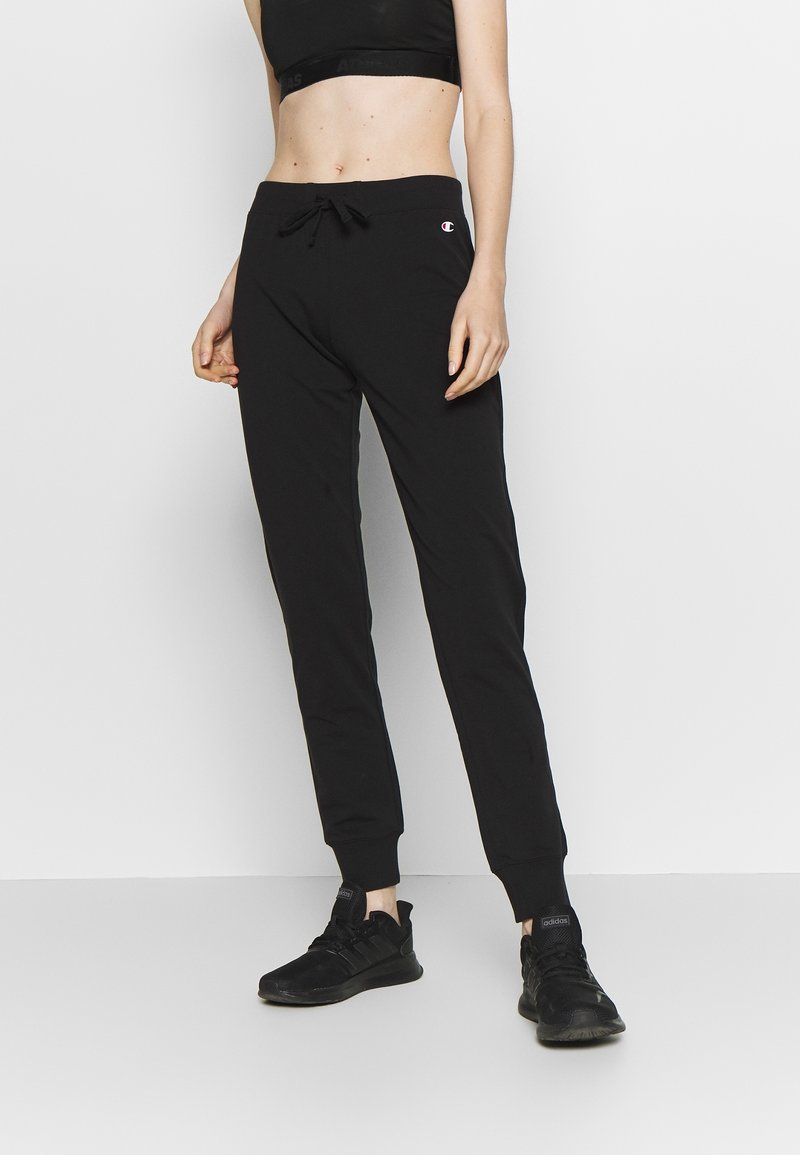 Schwarze Jogginghose mit Kordelzug in der Taille, verjüngten Bündchen und kleinem Markenlogo am linken Oberschenkel. Hergestellt aus weichem Baumwollstoff.