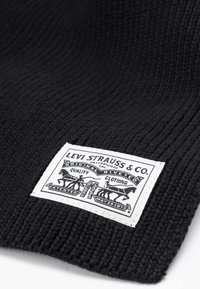 Berretto lavorato a maglia nero con un motivo testurizzato. Etichetta bianca con il testo "Levi Strauss & Co." e dettagli tipografici vintage con cavalli.