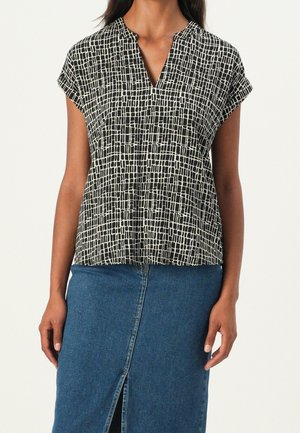 Kvinde iført kortærmet bluse i sort-hvidt ternet mønster med V-hals, stukket ned i en blå denimnederdel med forretsplit.