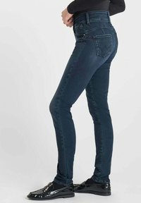 Jean skinny taille haute en denim foncé. Caractéristiques : texture lisse, poches arrière et fermeture à glissière à l'avant avec bouton.