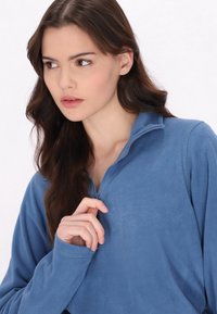 Pullover in pile azzurro chiaro con colletto a mezza zip, maniche lunghe e una texture morbida. Presenta una vestibilità rilassata e dettagli cuciti.