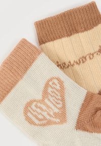 Ζευγάρι πλεκτές κάλτσες με κρεμ βάση και σχέδιο καρδιάς σε ανοιχτό καφέ, με ριγέ μανσέτα σε καφέ χρώμα. Υφάσματα με υφή, casual σχεδιασμός.