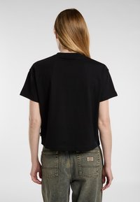 Must have lühikeste varrukatega must lühike t-särk, millel on ümmargune kaelus. Kombineeritud kõrge vöökohtadega, kulunud denimpükstega, millel on klassikaline taskute kujundus.