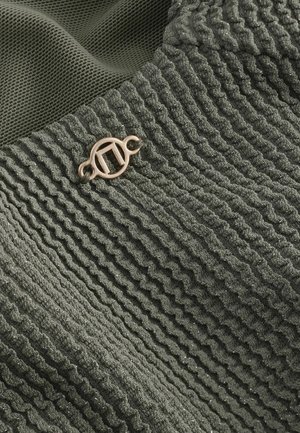 Țesătură verde texturată cu dungi ondulate, având un mic accent cu logo din bronz. Materialul are un luciu subtil și un aspect moale.