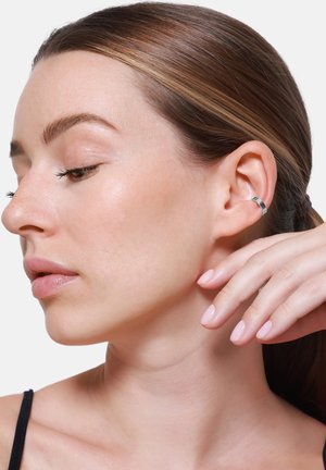 Zilveren oorring met een gladde, gepolijste afwerking, te zien op een oor. Huidtint is licht, met natuurlijke make-up en steil bruin haar.