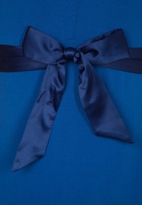 Niebieski kobaltowy strój o gładkiej fakturze, z ciemnoniebieską satynową kokardą związaną w talii, podkreślająca elegancję w designie.