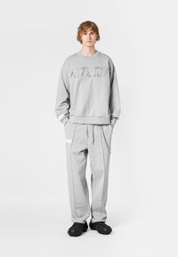 Sudadera gris con detalle de logo, combinada con joggers grises a juego que cuentan con un bolsillo lateral y un acento de cadena. Tejido texturizado y ajuste relajado.