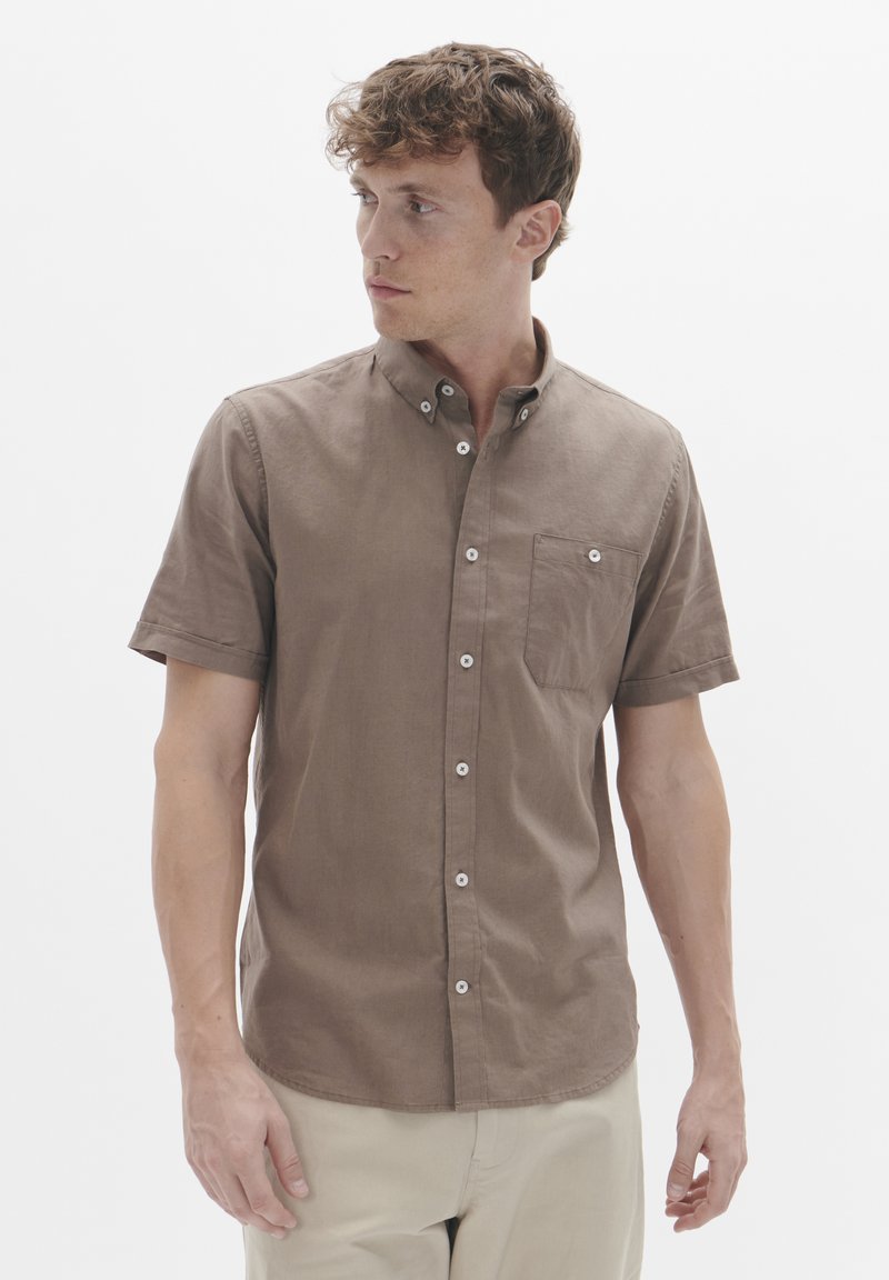Camisa de botones de manga corta en color marrón con cuello, un bolsillo en el pecho y botones blancos. La tela parece suave con una textura lisa.