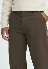 Brune bomuldsbukser med en glat tekstur og lige ben-design. Har frontlommer og en mellemhøj talje. Minimale syningdetaljer.