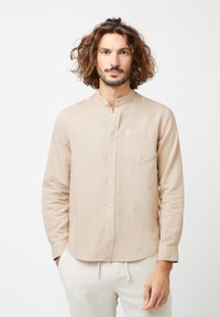 Lichtbeige, lange mouwen shirt met een bandkraag, knopen aan de voorkant en een borstzak. Zachte stof met een gladde textuur.