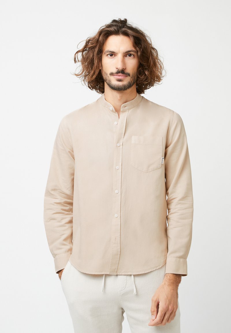 Lichtbeige, lange mouwen shirt met een bandkraag, knopen aan de voorkant en een borstzak. Zachte stof met een gladde textuur.