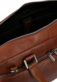 Borsa in pelle marrone con finitura testurizzata, dotata di chiusura a zip argentata, accessori metallici e forma rettangolare; l'interno presenta una fodera in tessuto nero.